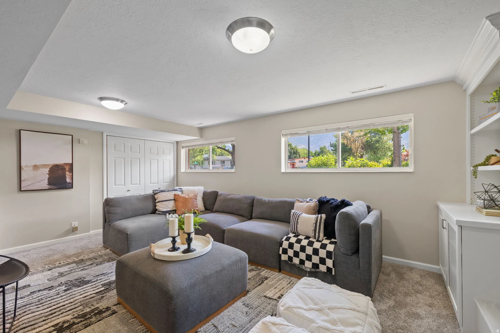 Carpeted lower-level living area featuring two windows, recessed lighting, built-in shelving, and bifold closet doors