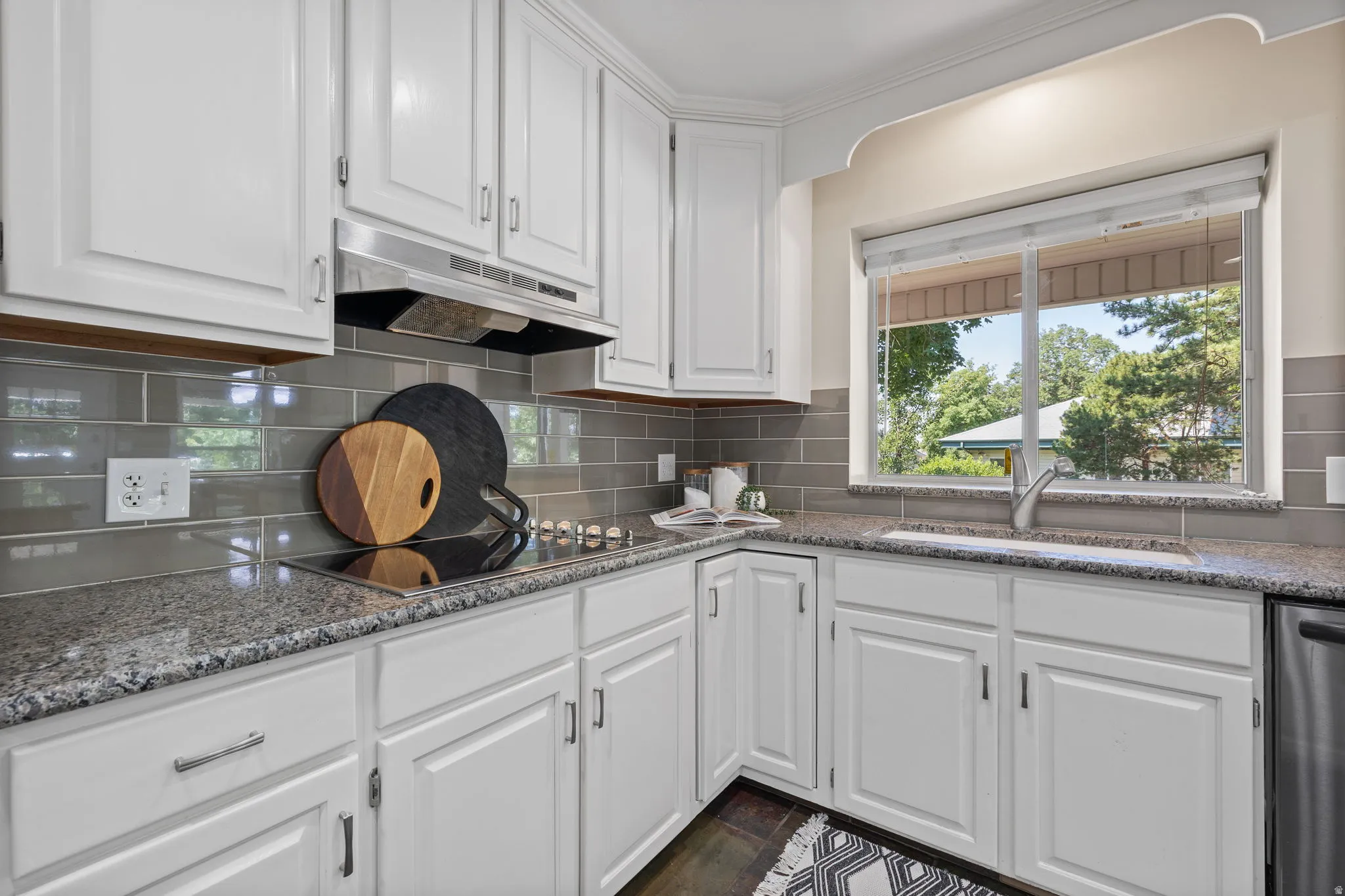 Kitchen featuring white cabinetry, grey subway tile backsplash, speckled countertops, and a window above the sink