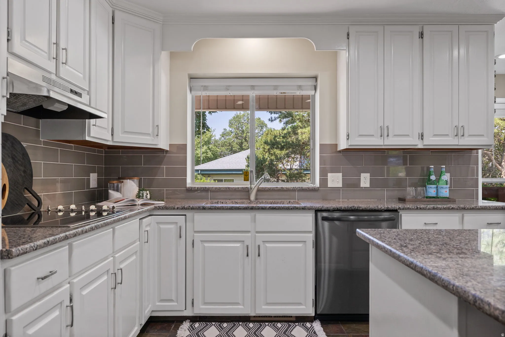 White cabinetry throughout the kitchen, featuring a built-in stainless steel dishwasher, glass cooktop, and a tile backsplash