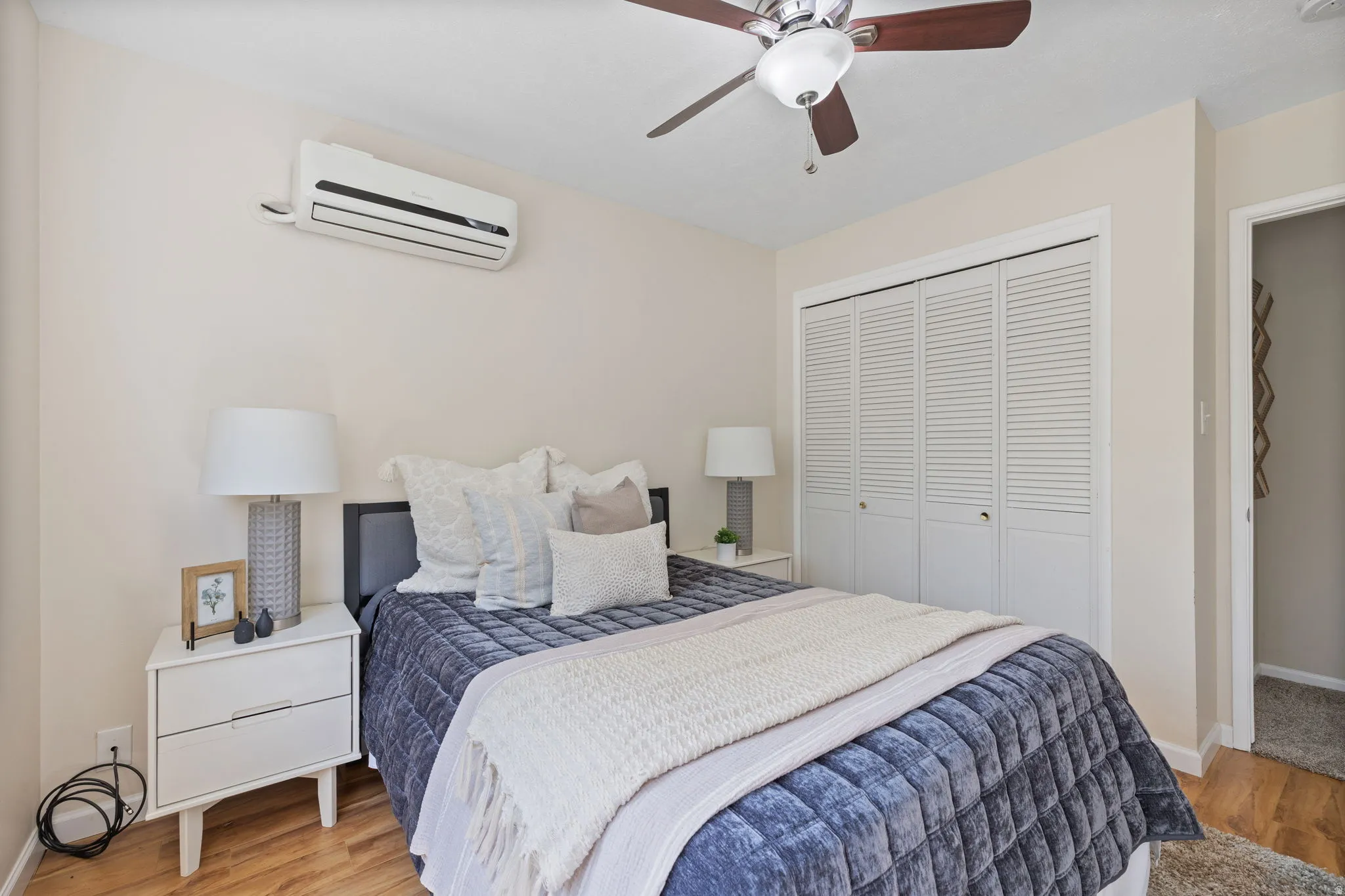 Bedroom featuring wood-finish flooring, a wall-mounted mini-split air conditioning unit, and a ceiling fan with integrated lighting