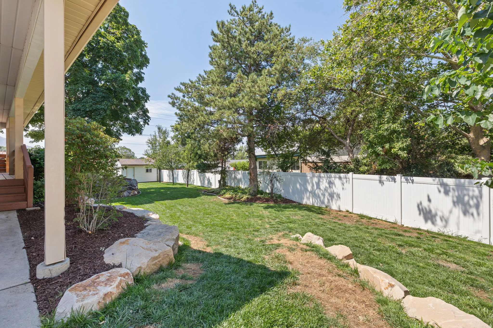 Expansive backyard featuring a manicured lawn, established trees, and a white privacy fence