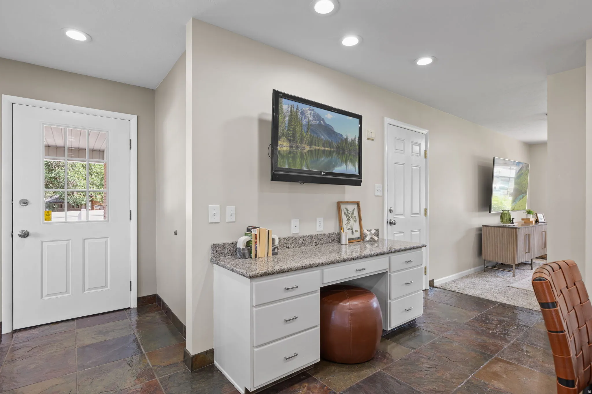 Built-in desk area featuring a granite countertop, white cabinetry with silver hardware, and slate tile flooring