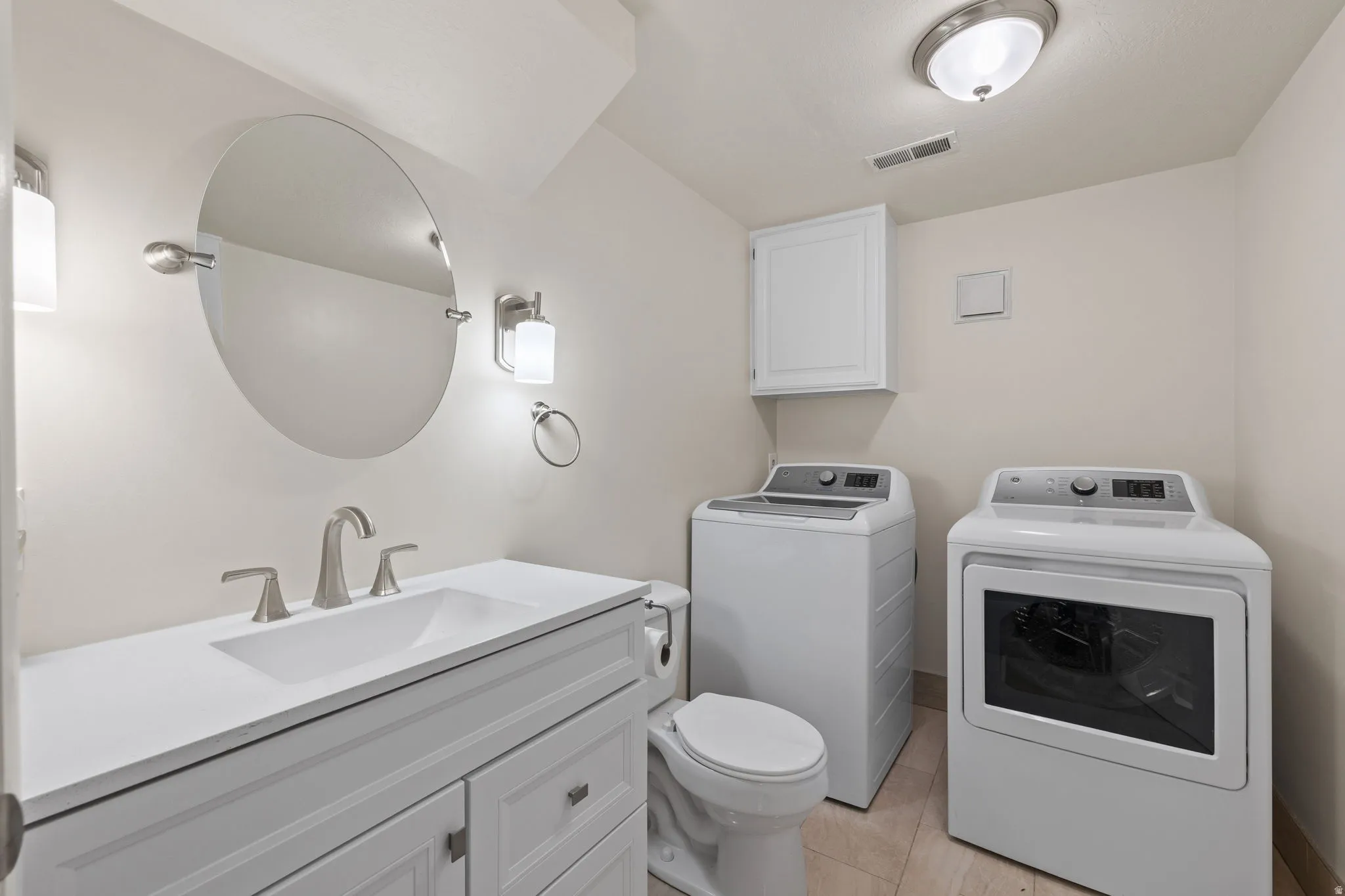 Laundry room featuring a white vanity with integrated sink, brushed nickel fixtures, an oval mirror, and a toilet