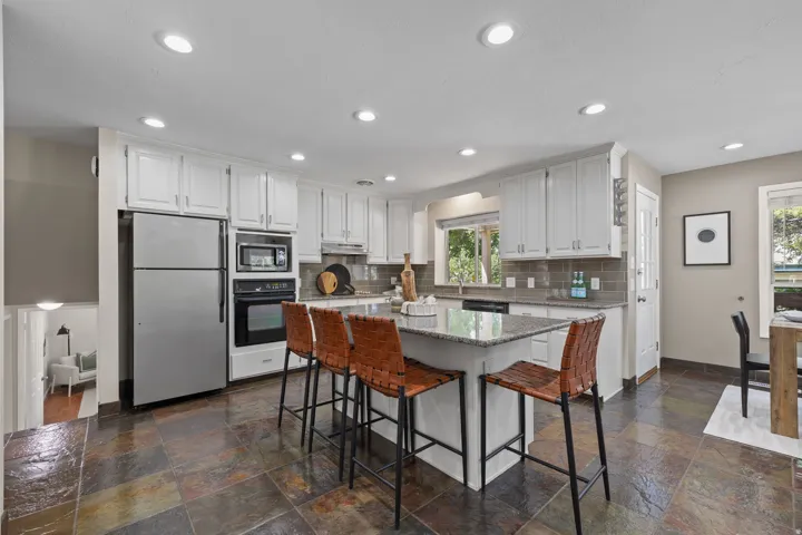Kitchen featuring an island with stone countertop, white cabinetry, integrated stainless steel appliances, a tile backsplash, and multi-toned slate flooring