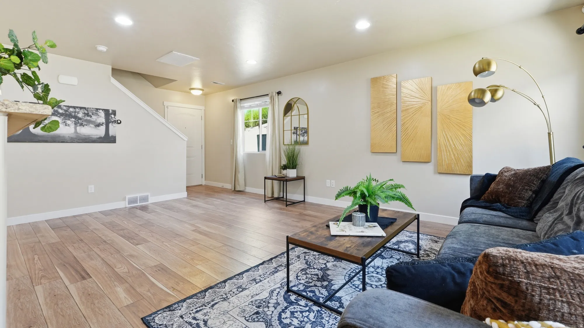 Open-concept living area featuring wood-finish flooring, recessed lighting, a window with natural light, and a staircase with a white railing