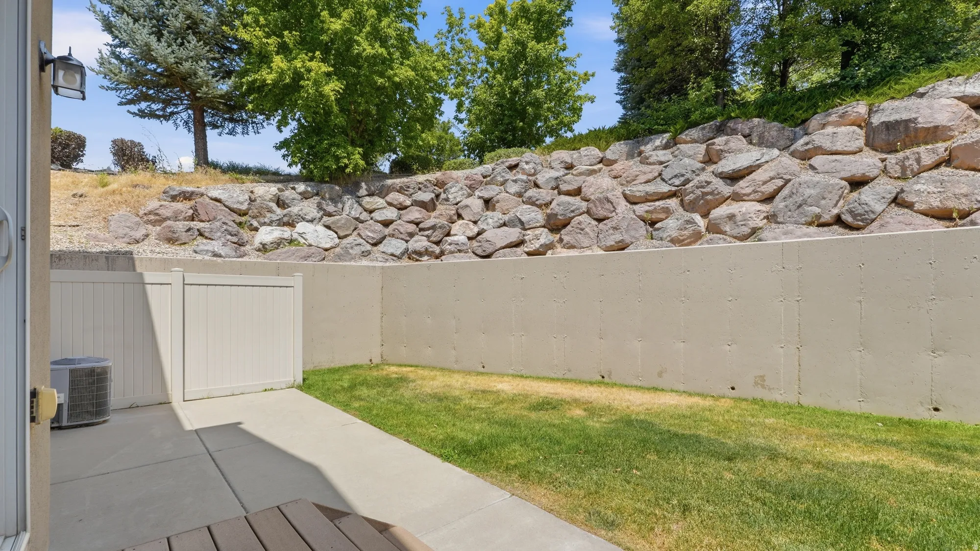 Private patio area featuring a concrete slab, a patch of green lawn, and a stone retaining wall