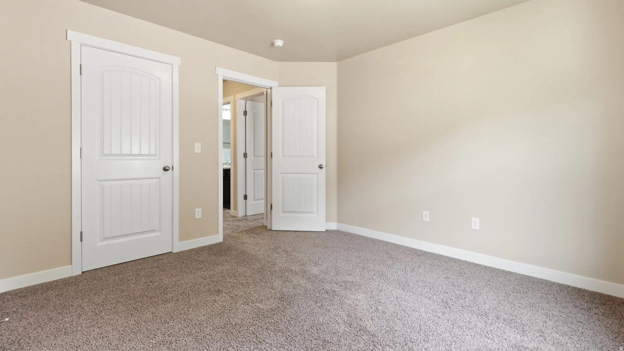 Neutral-toned interior room featuring light beige wall paint, white trim, and textured carpet flooring