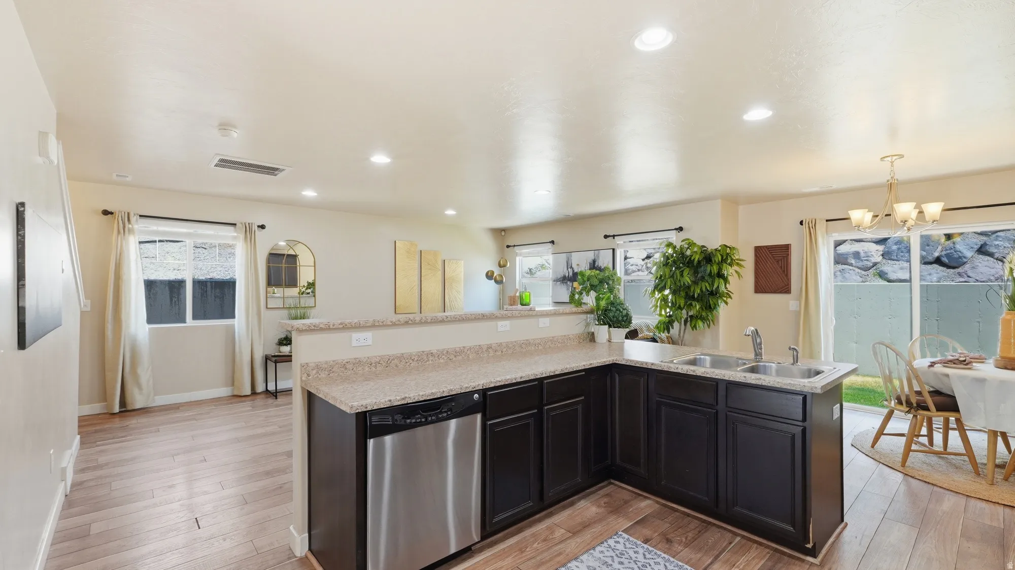 Open-concept living space featuring wood-finish flooring, a kitchen with dark cabinetry and stainless steel appliances, a breakfast bar, and a dining area with direct outdoor access via sliding glass doors