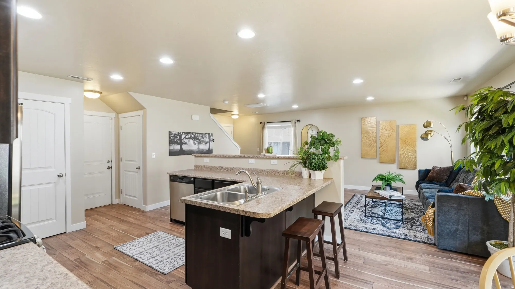 Open-concept living area featuring wood-finish flooring throughout, recessed lighting, and a kitchen island with a double basin sink