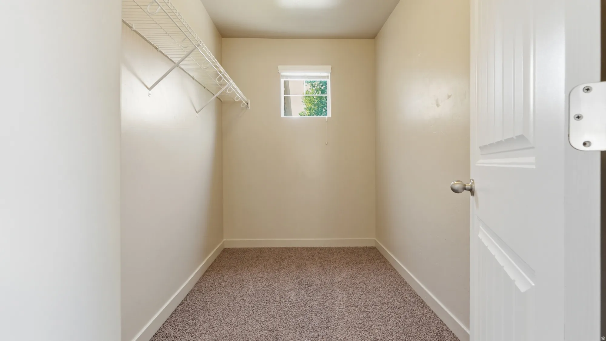 Walk-in closet featuring light beige wall paint, white trim, a small window with a white blind, and a wire shelving system