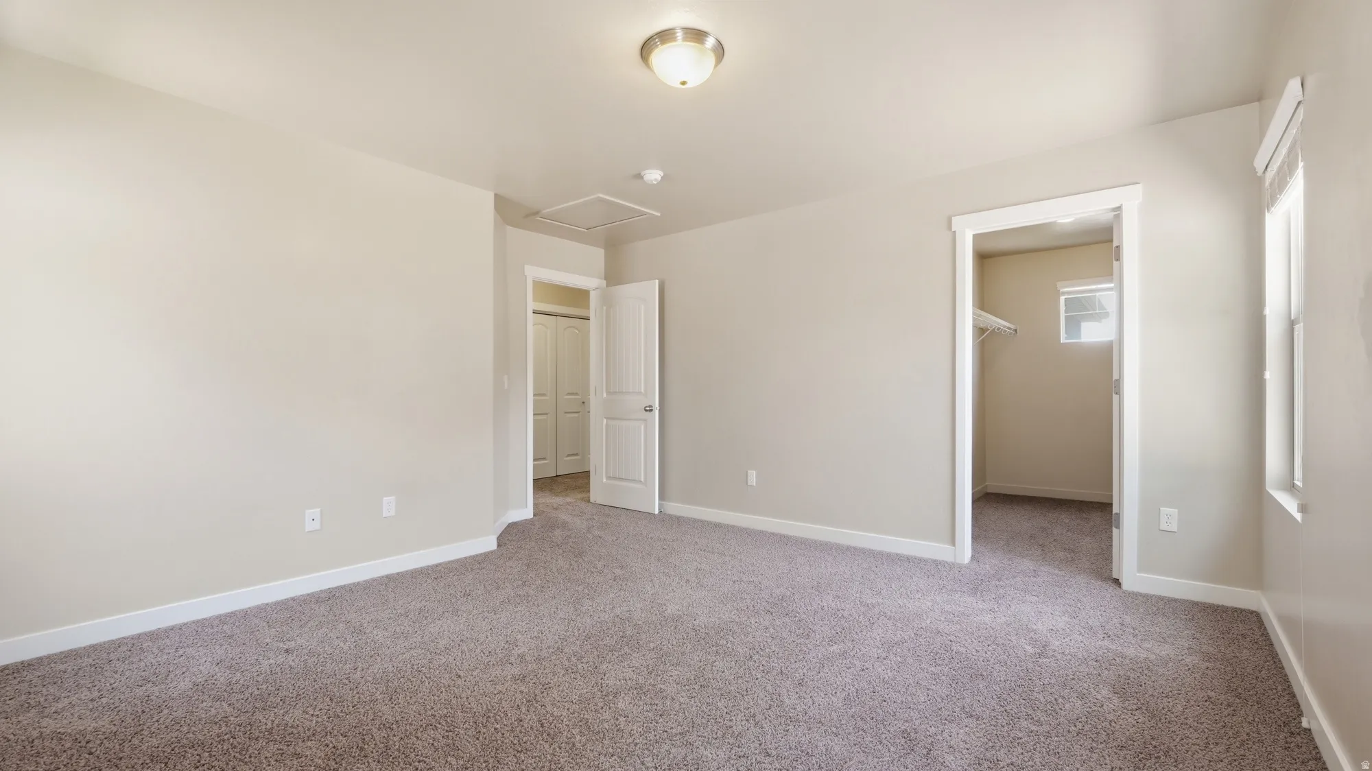 Spacious room featuring neutral carpet flooring, light-toned walls, a flush-mount ceiling light fixture, and two doorways leading to additional areas