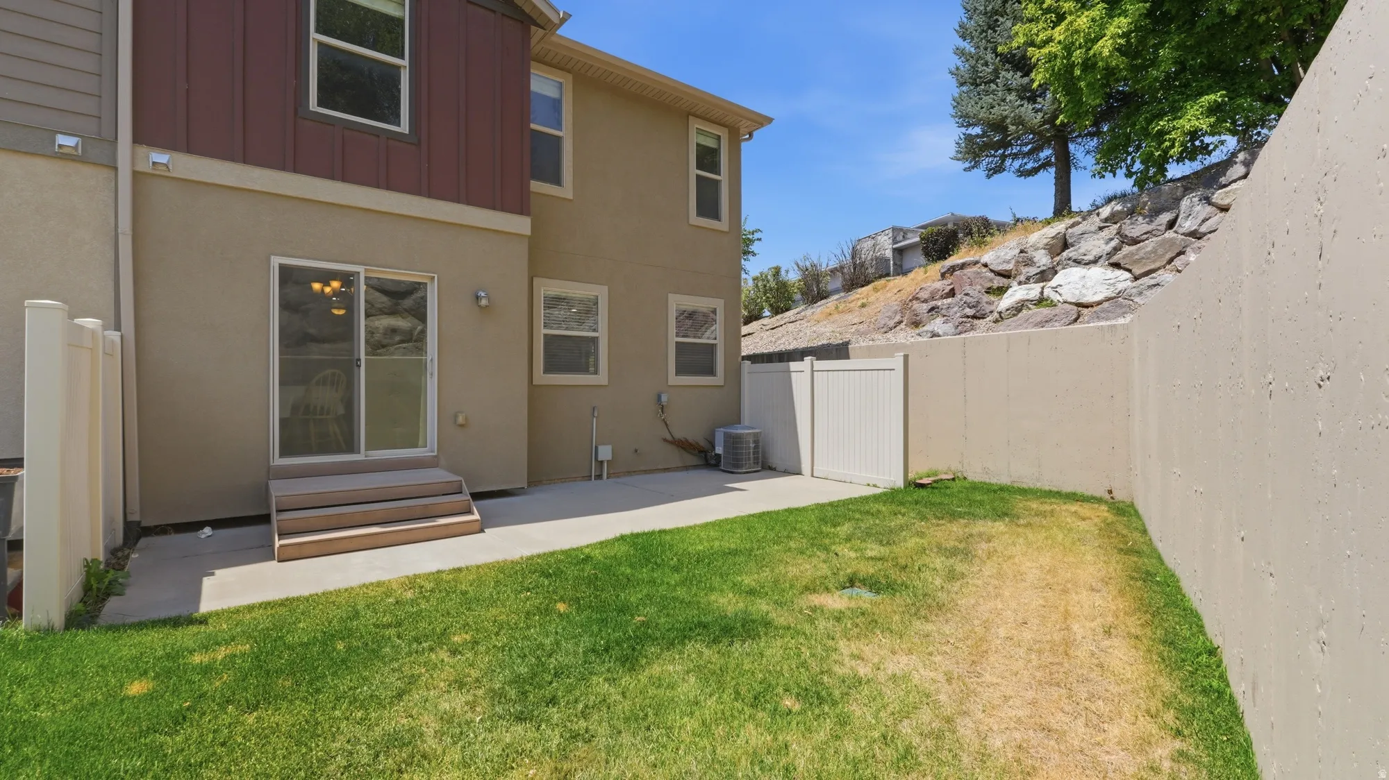 Private backyard featuring a concrete patio, grassy areas, and a multi-level retaining wall