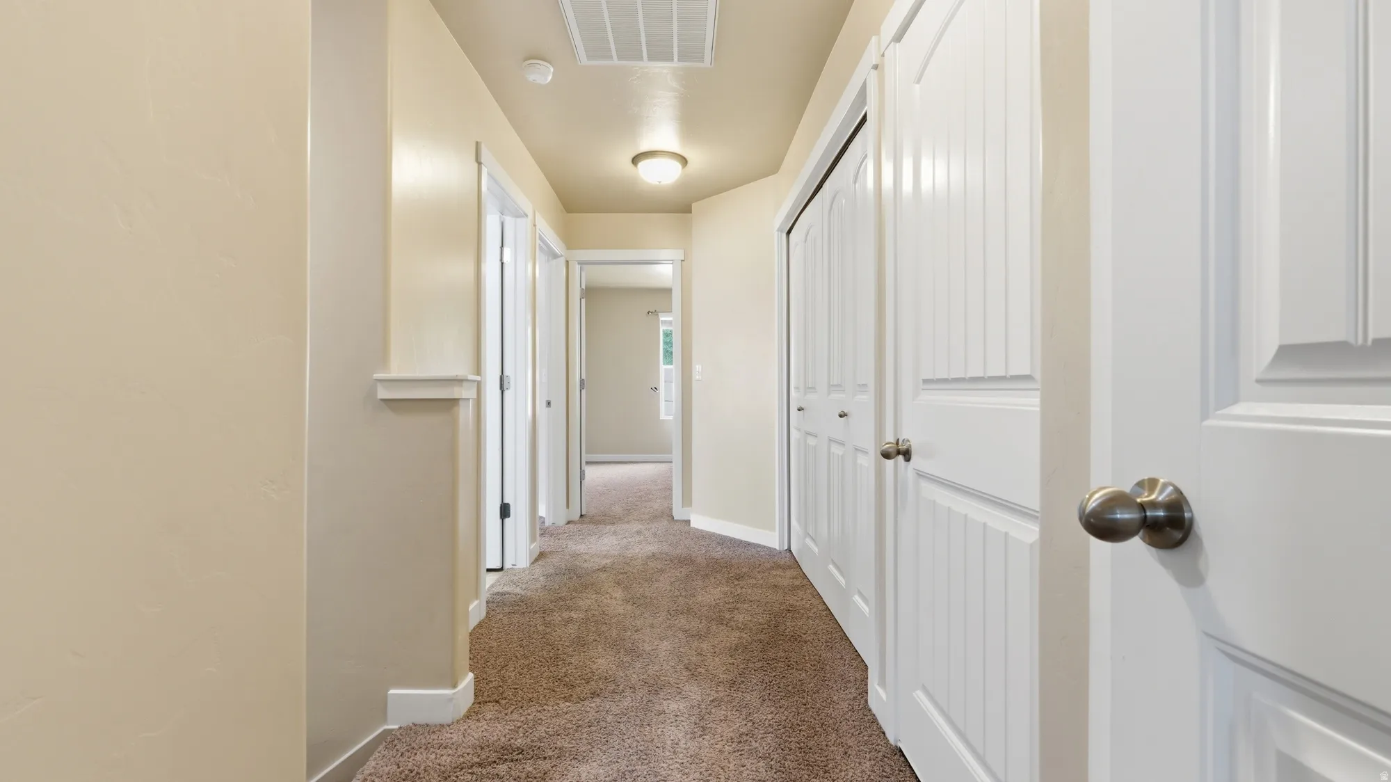 Hallway featuring light beige walls, carpeted flooring, multiple white paneled doors with brushed nickel hardware, and recessed lighting