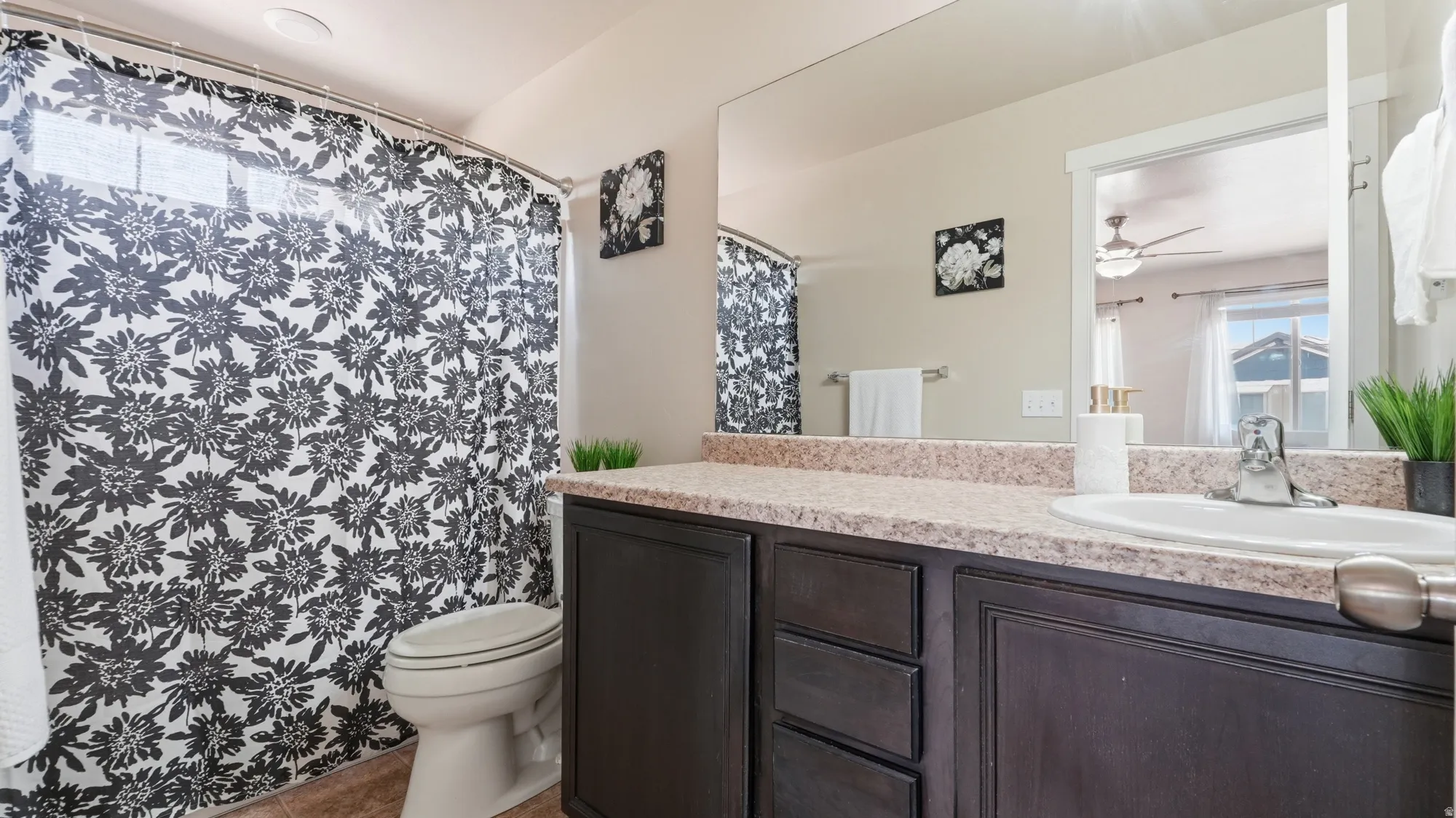 Bathroom featuring a dark wood-finish vanity with a single basin sink, a large wall-mounted mirror, and a shower-over-tub combination with a window