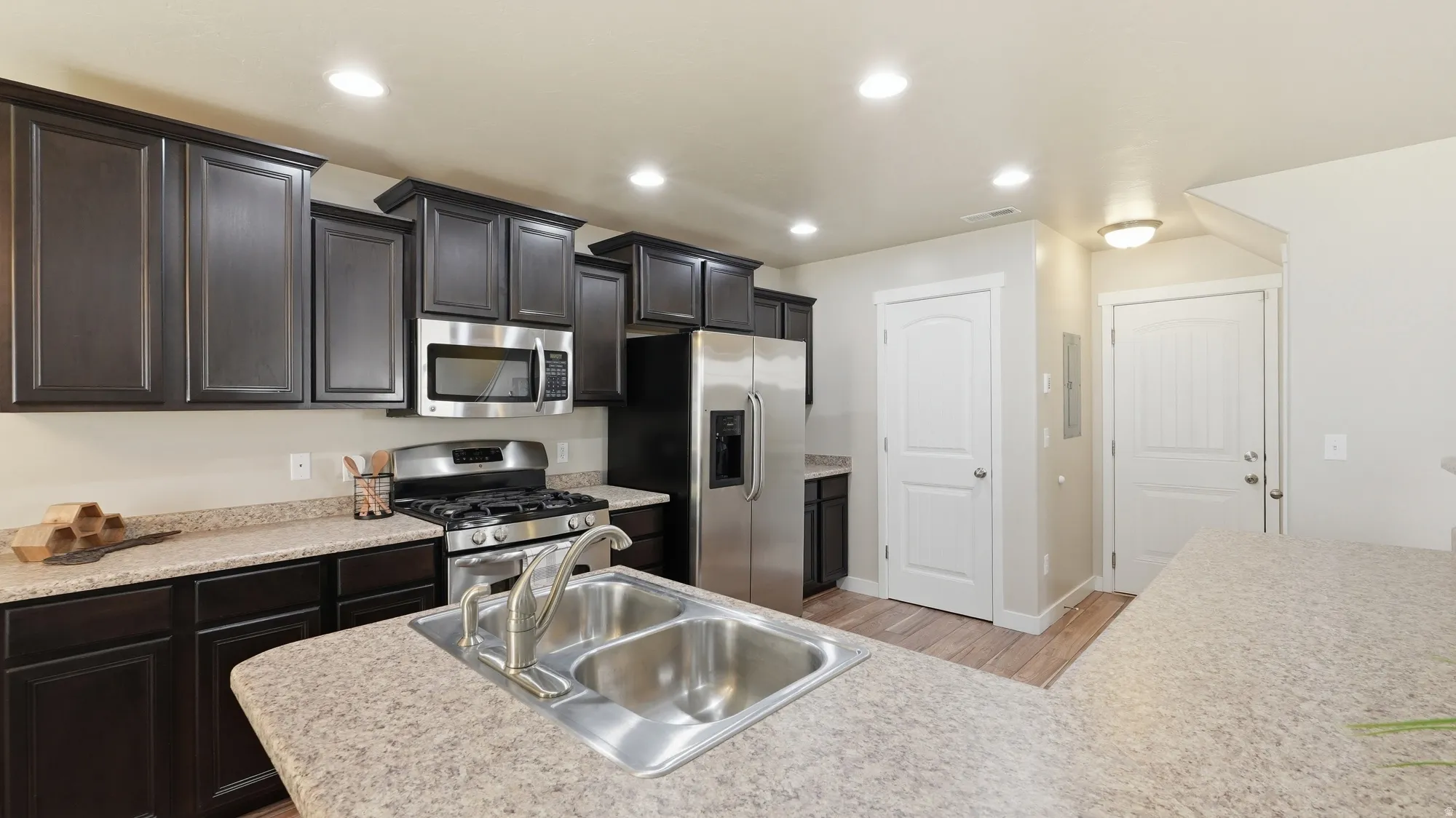 Kitchen featuring dark wood-finish cabinetry, speckled countertops, and stainless steel appliances including a gas range and microwave