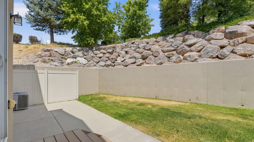 Private patio area featuring a concrete slab, a patch of green lawn, and a stone retaining wall