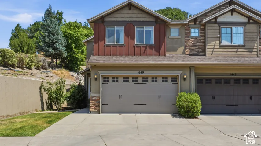 Two-story residence featuring a two-car garage with carriage-style doors, stone veneer accents, and vertical siding