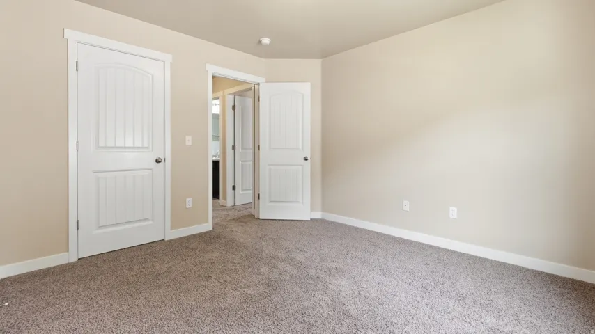 Neutral-toned interior room featuring light beige wall paint, white trim, and textured carpet flooring