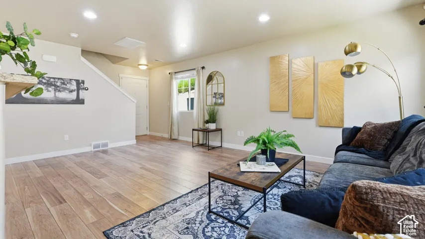 Open-concept living area featuring wood-finish flooring, recessed lighting, a window with natural light, and a staircase with a white railing