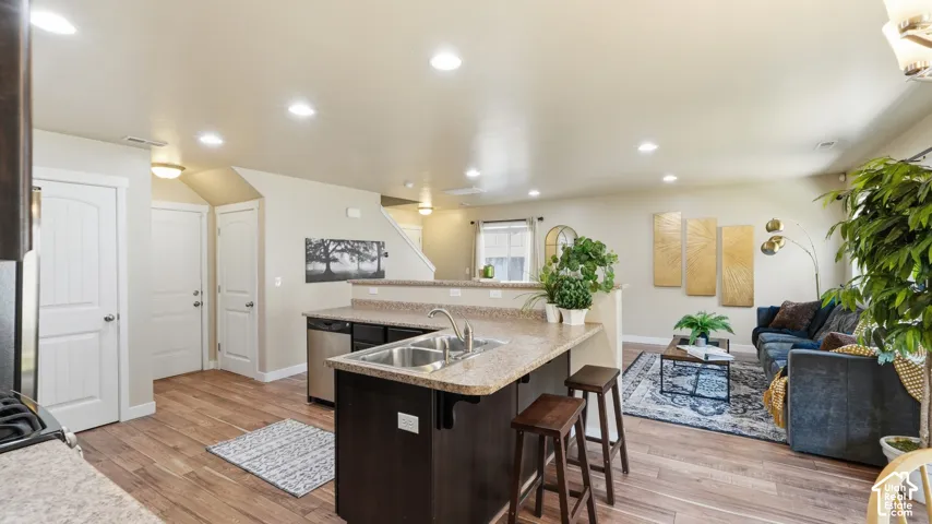 Open-concept living area featuring wood-finish flooring throughout, recessed lighting, and a kitchen island with a double basin sink