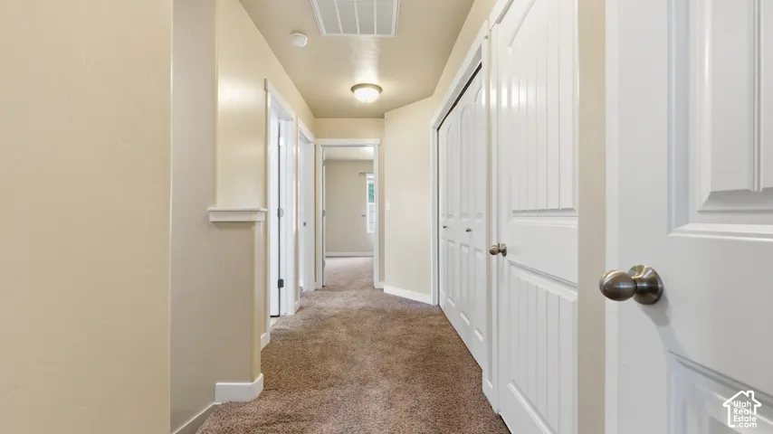 Hallway featuring light beige walls, carpeted flooring, multiple white paneled doors with brushed nickel hardware, and recessed lighting