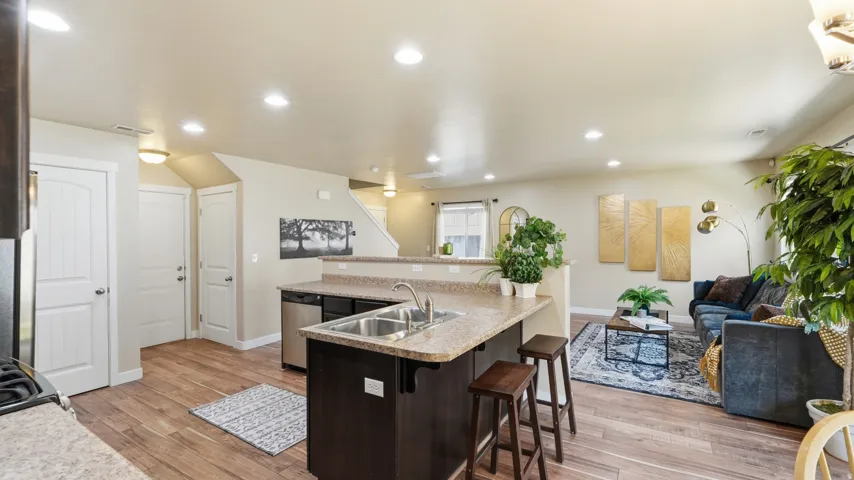 Open-concept living area featuring wood-finish flooring throughout, recessed lighting, and a kitchen island with a double basin sink
