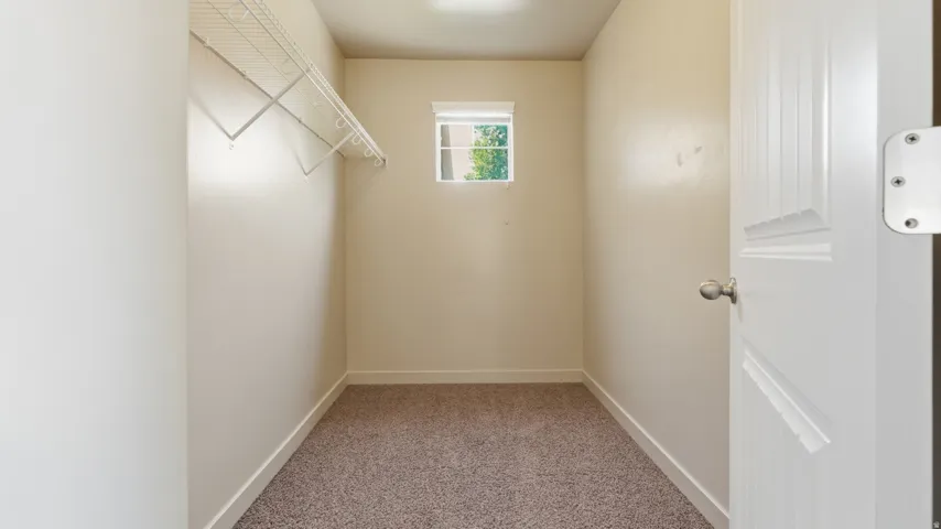 Walk-in closet featuring light beige wall paint, white trim, a small window with a white blind, and a wire shelving system
