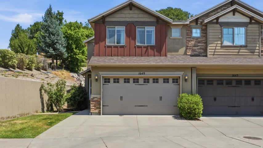 Two-story residence featuring a two-car garage with carriage-style doors, stone veneer accents, and vertical siding