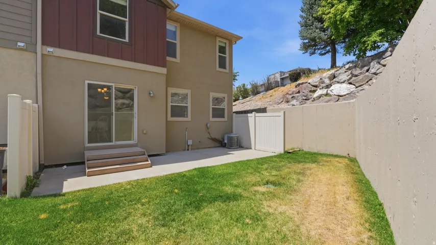 Private backyard featuring a concrete patio, grassy areas, and a multi-level retaining wall