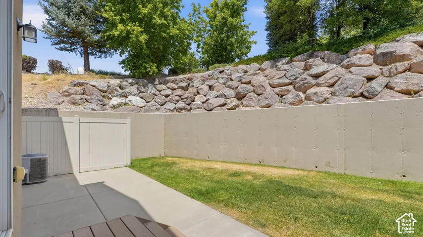 Private patio area featuring a concrete slab, a patch of green lawn, and a stone retaining wall