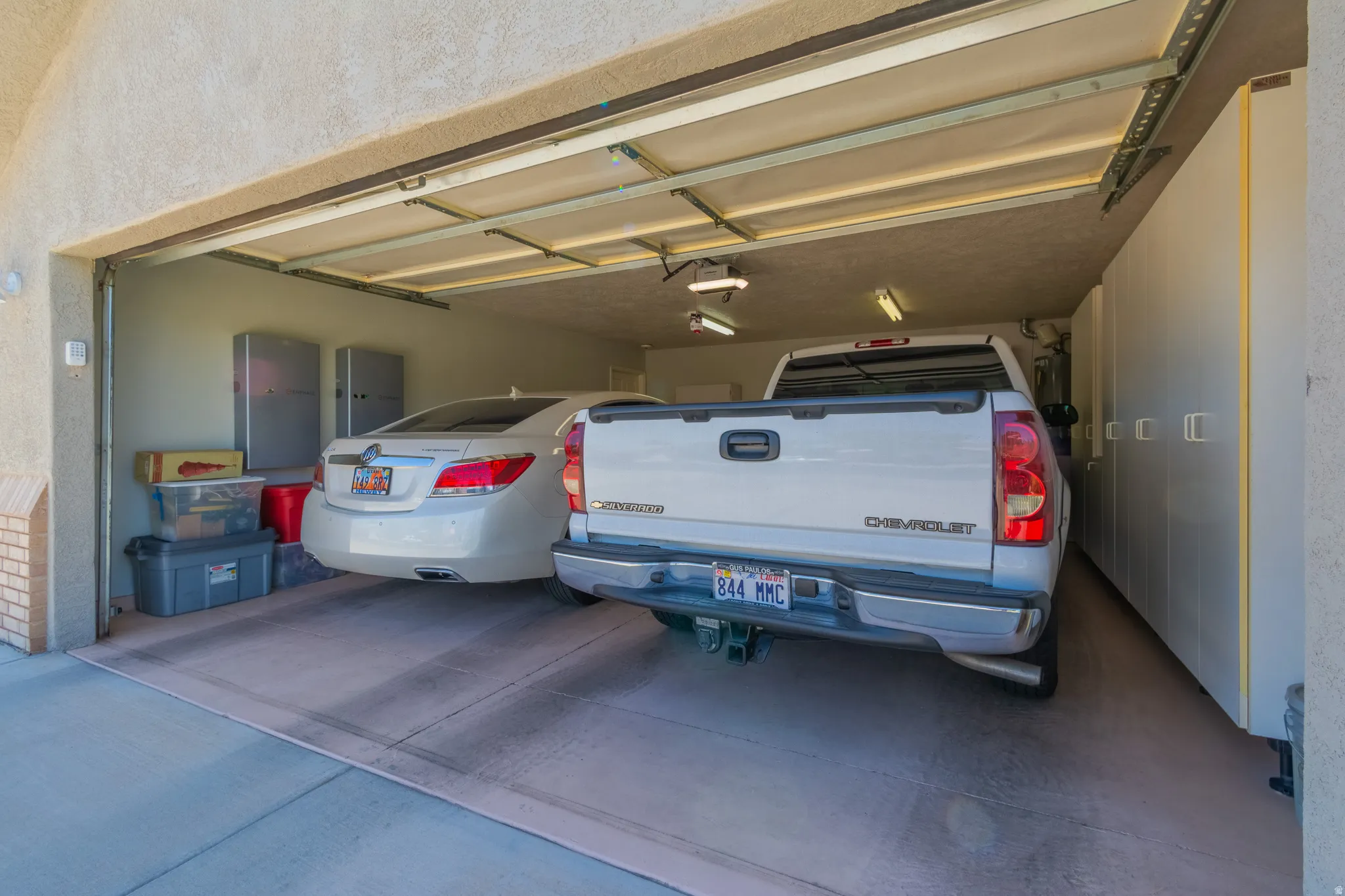 Spacious two-car garage featuring a textured concrete floor, overhead fluorescent lighting, and extensive built-in cabinetry along one wall