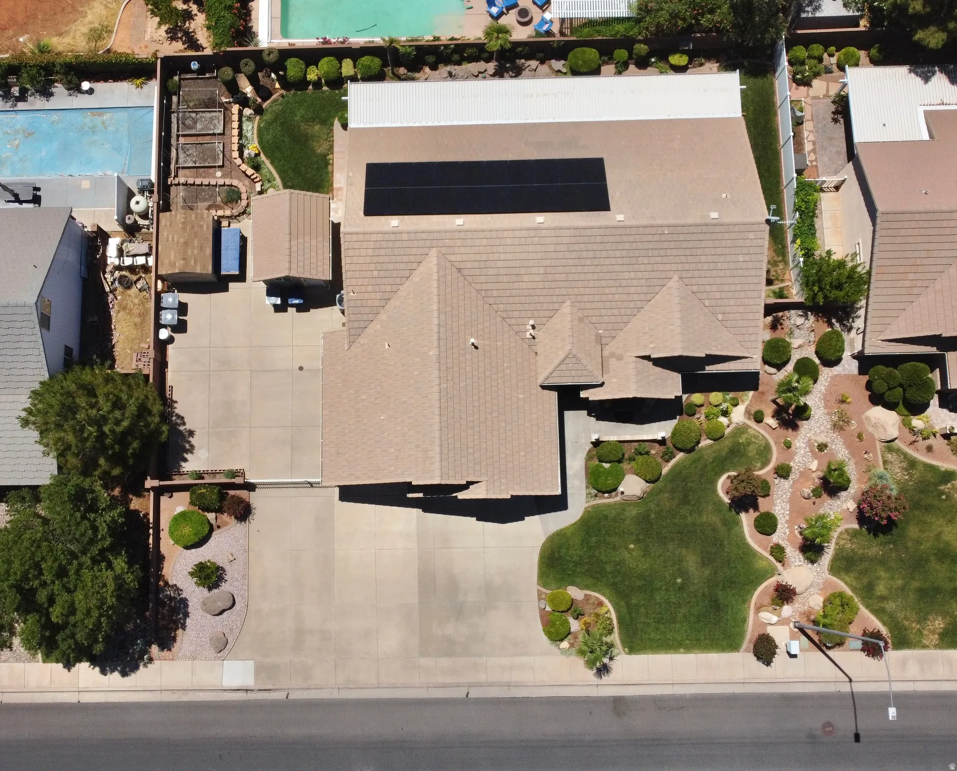 Aerial perspective highlighting a multi-peaked roofline, an expansive paved driveway, and a meticulously landscaped front yard with varied plantings