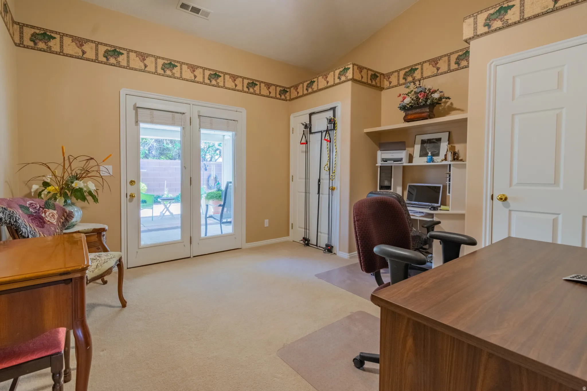 Room featuring French doors opening to an outdoor patio, built-in shelving, a vaulted ceiling, and neutral carpet flooring