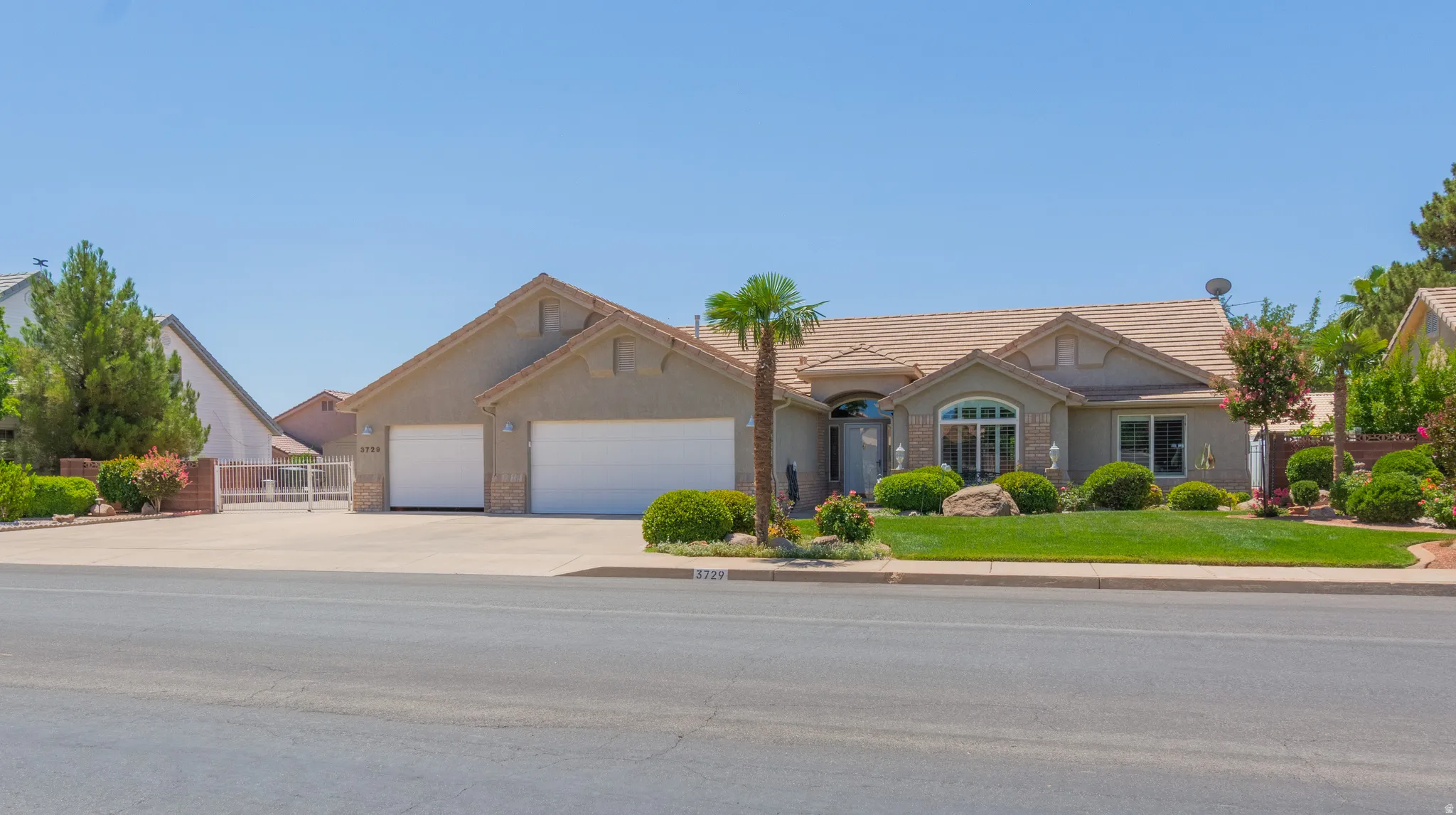 Stucco exterior with a tiled roof, two-car garage, manicured front lawn, mature landscaping, and an arched entry with a decorative front door