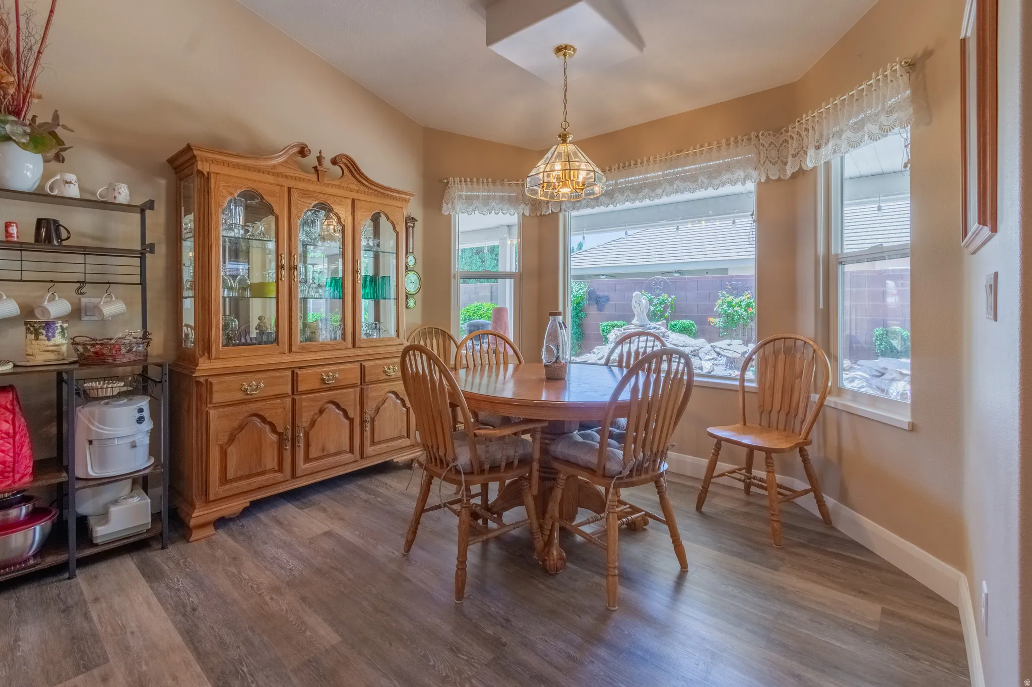 Dining area featuring wood-finish flooring, a tray ceiling with a chandelier, and a bay window overlooking a landscaped backyard