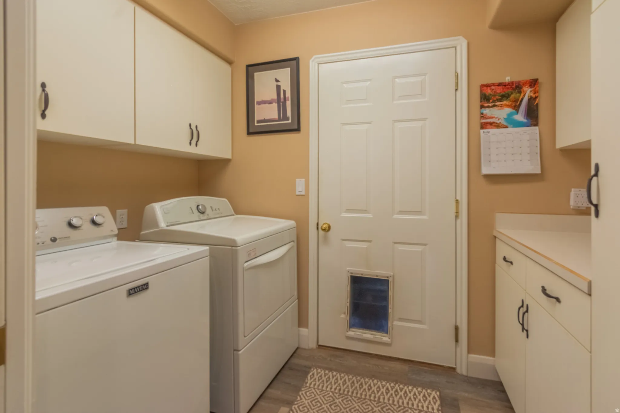 Laundry room featuring upper and lower cabinetry, ample countertop space, and wood-finish flooring