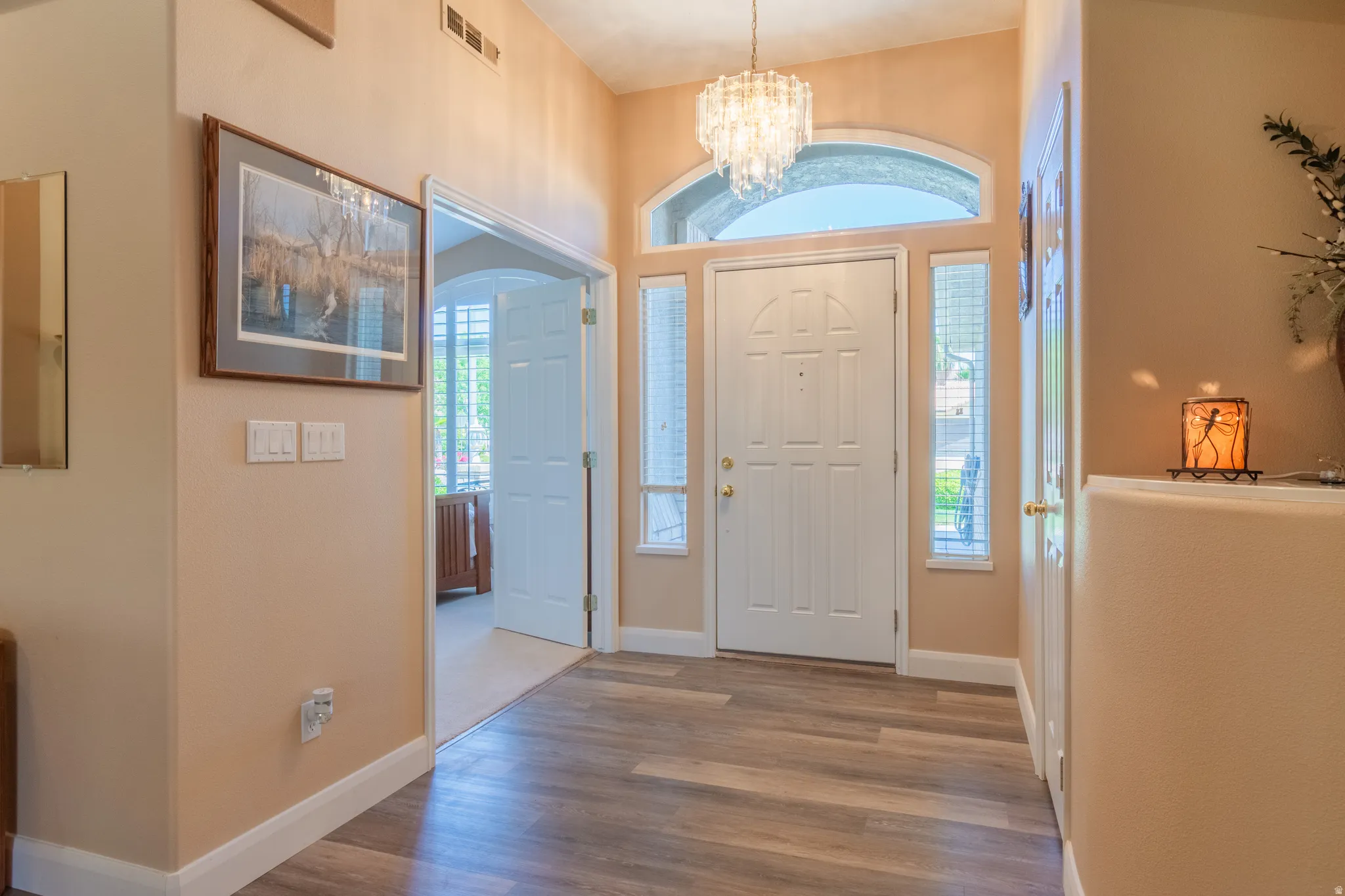 Foyer featuring wood-finish flooring, a white paneled entry door with sidelights and an arched transom, and a crystal chandelier