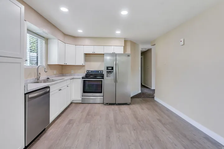 Kitchen featuring white cabinetry, stainless steel appliances, speckled countertops, a double basin sink with a gooseneck faucet, and wood-finish flooring