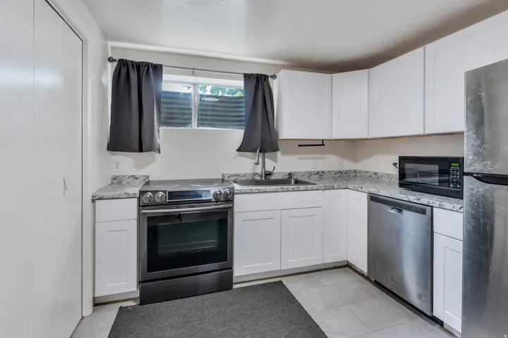 Kitchen featuring white cabinetry, light-toned countertops, tile flooring, and stainless steel appliances