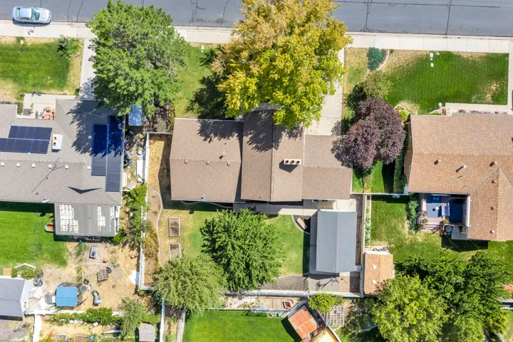 Brown shingle roofing, paved driveway, mature trees, landscaped lot, and privacy fencing