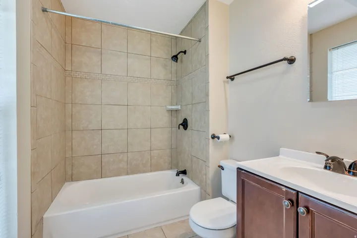 Bathroom featuring a white bathtub, ceramic tile shower surround with decorative accent, dark wood-finish vanity, and bronze-finish fixtures