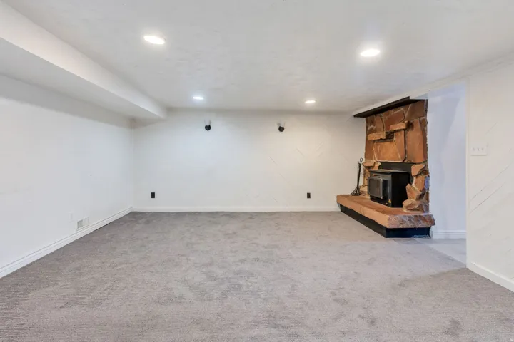 Spacious room featuring gray carpeting, recessed ceiling lighting, and a stone-clad fireplace with a hearth