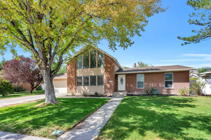 Brick exterior residence featuring a prominent gabled front section with large windows, a white entry door, an attached garage, and a concrete pathway leading to the entrance