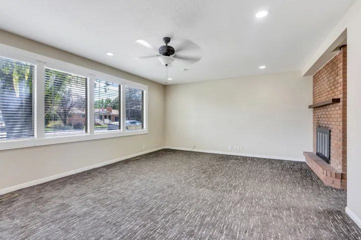 Spacious living area featuring a brick fireplace with a wood mantle, a ceiling fan, recessed lighting, and large windows with blinds