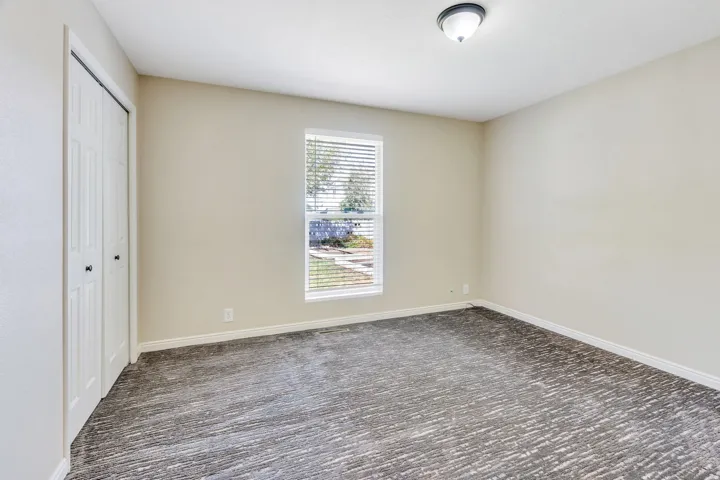 Neutral wall finishes, textured carpeting, a window with blinds, and bi-fold closet doors