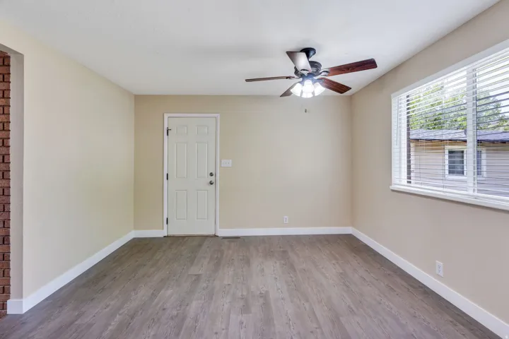 Wood-finish flooring, ceiling fan with integrated lighting, brick accent wall, and a multi-pane window with blinds