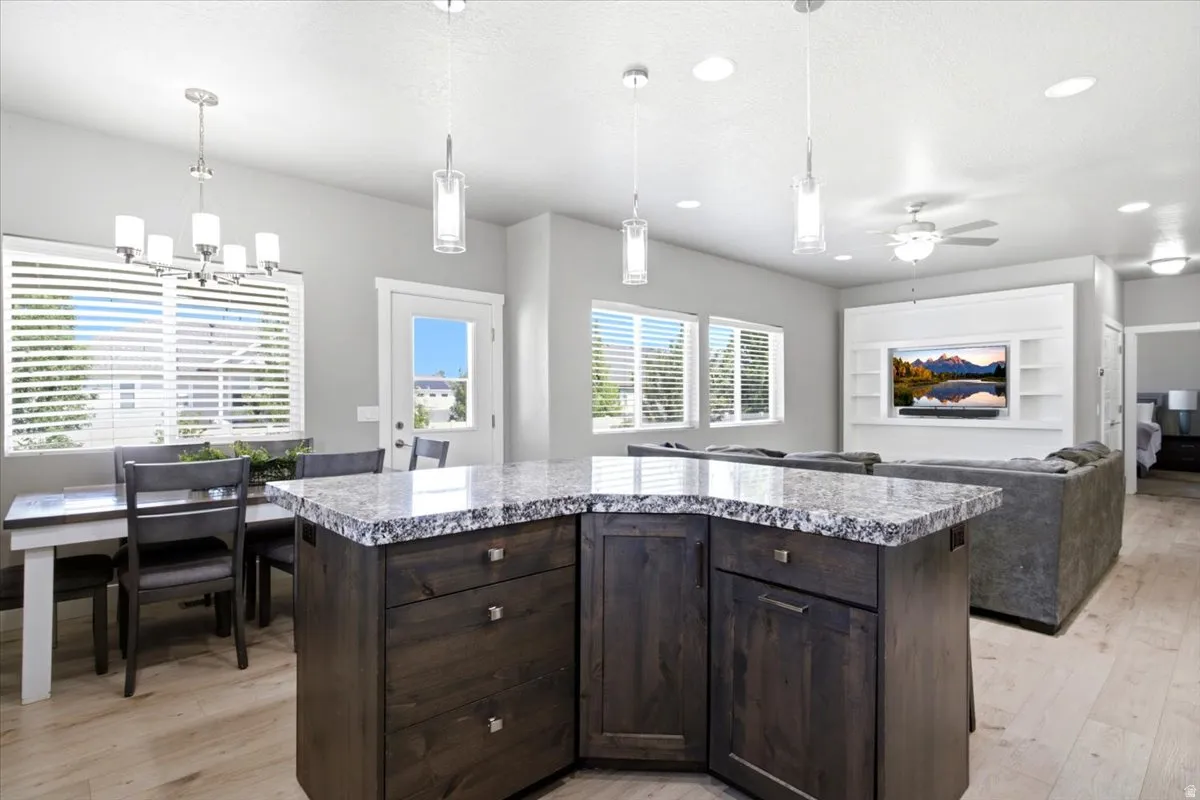 Kitchen island with granite countertop and dark wood-finish cabinetry, illuminated by pendant lighting