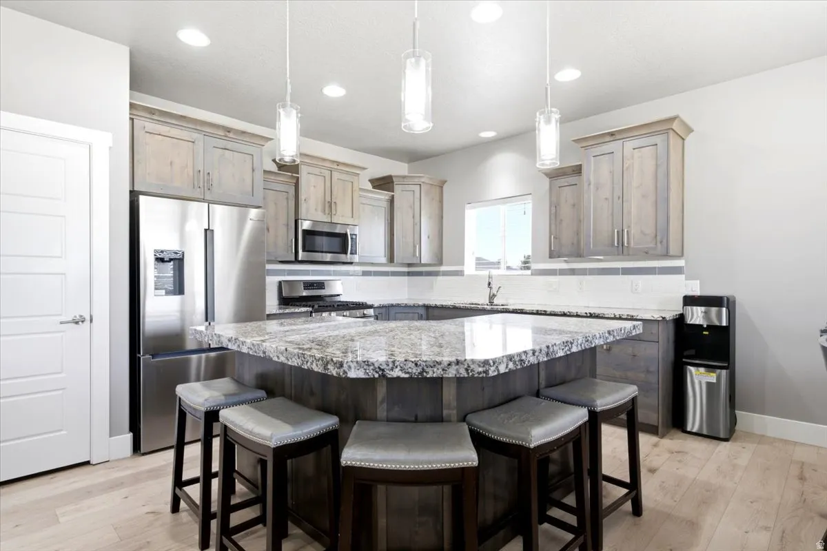 Gourmet kitchen featuring a large island with a speckled countertop, light wood-finish cabinetry, stainless steel appliances, and pendant lighting