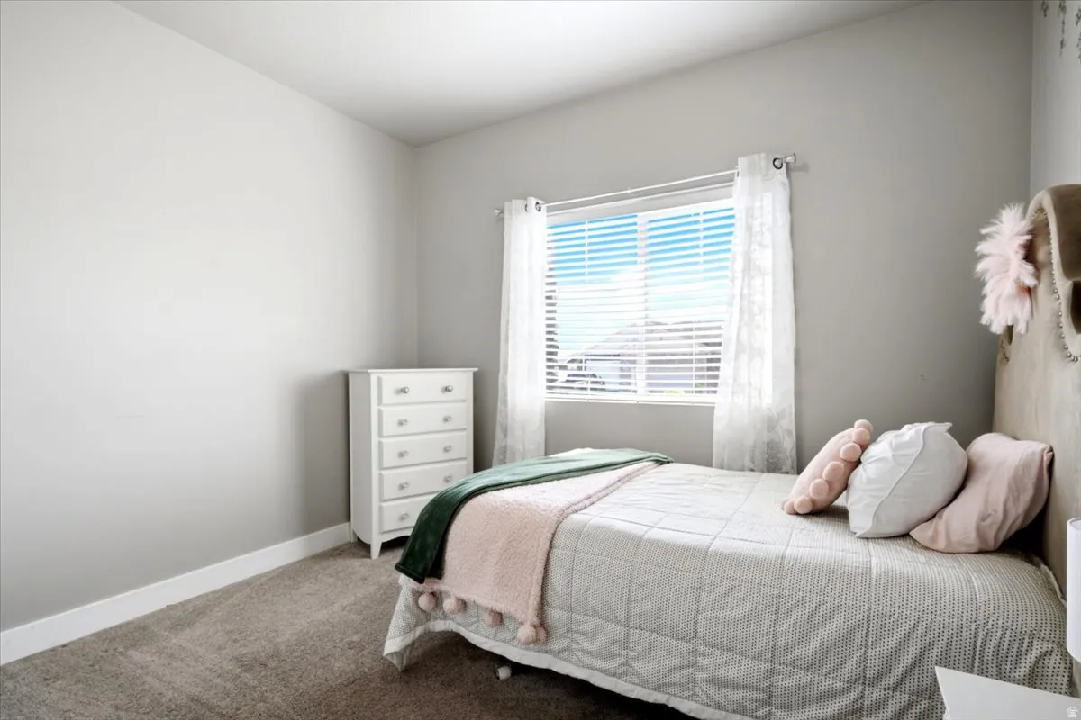 Bedroom featuring neutral-toned walls, a single window with white blinds and sheer curtains, and gray carpeting