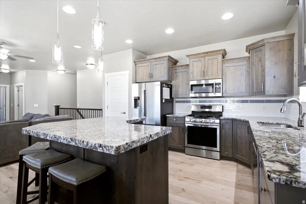 Open-concept kitchen featuring an island with stone countertops, stainless steel appliances, wood-finish flooring, recessed lighting, and pendant fixtures